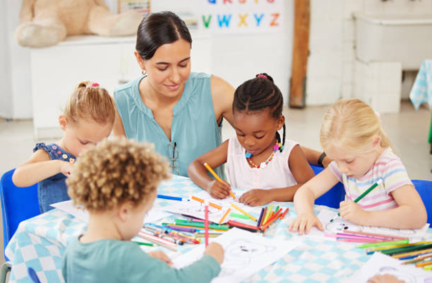 An early-childhood teacher working with four young children on letter and shape learning cards at a classroom table