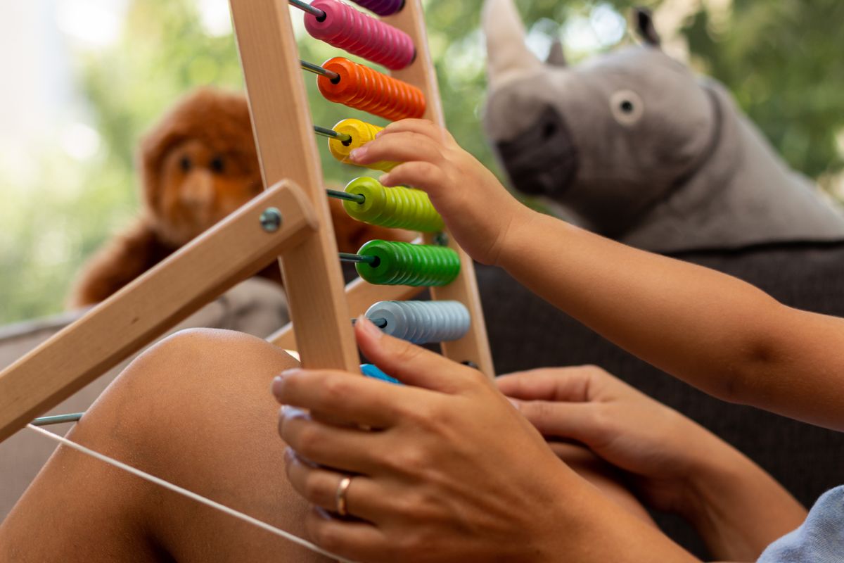 A parent and their young child counting together on a wooden abacus